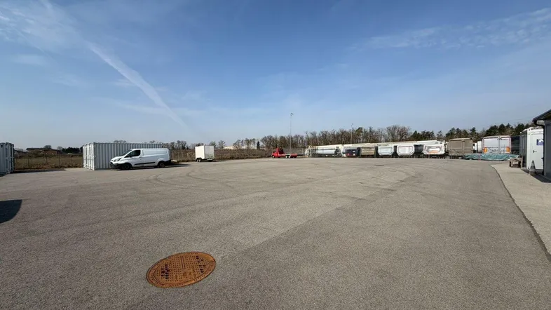 Großer asphaltierter Parkplatz mit mehreren Fahrzeugen und Containern unter blauem Himmel.