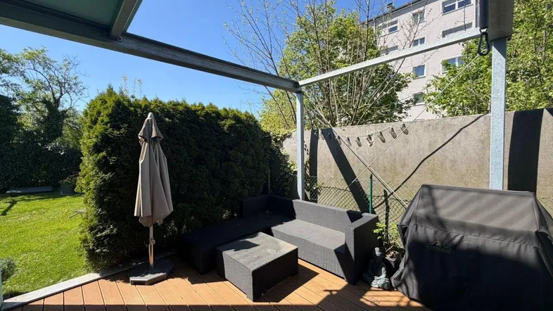 Gemütliche Terrasse mit Holzdeck, Gartenmöbeln und Grillbereich, umgeben von Grün.