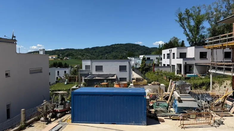 Baustelle mit modernen Häusern im Hintergrund und einem blauen Container unter klarem Himmel.