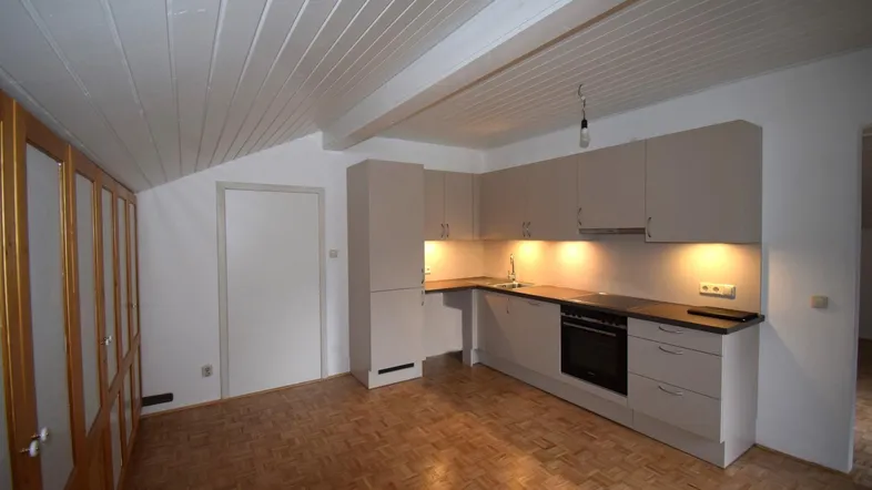 Kleine Einbauküche mit beigen Schränken, Holzbalkendecke und Parkettboden in einem Dachgeschossraum.