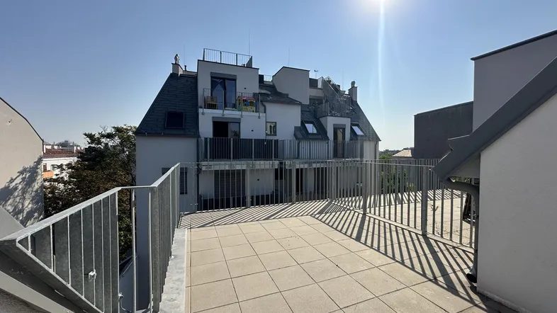 Große geflieste Dachterrasse mit Metallgeländer und sonnigem Ausblick auf das Gebäude.