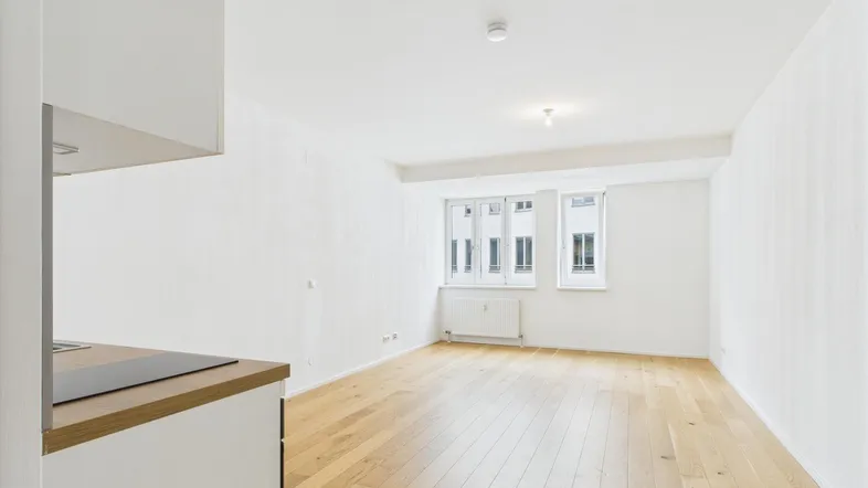 Helles Wohnzimmer mit Parkettboden und integrierter Küchenzeile, ideal für ein Studio-Apartment.