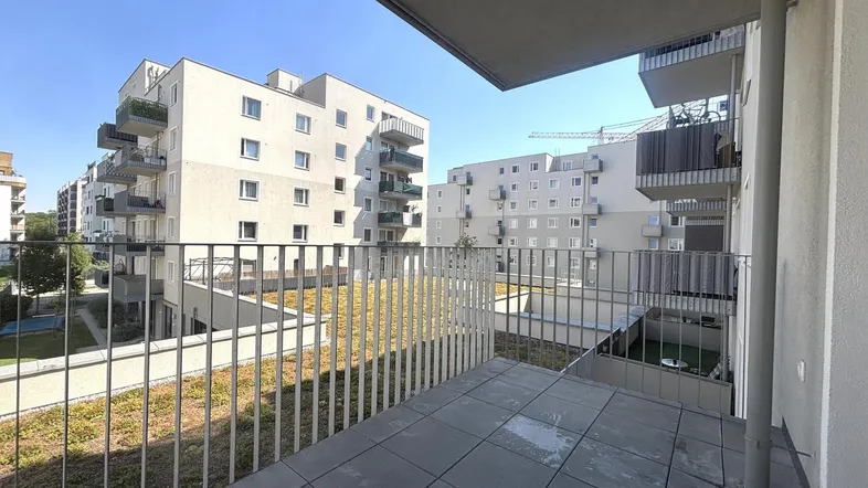 Geräumiger Balkon mit Fliesenboden und Blick auf moderne Wohngebäude mit begrünten Dächern.