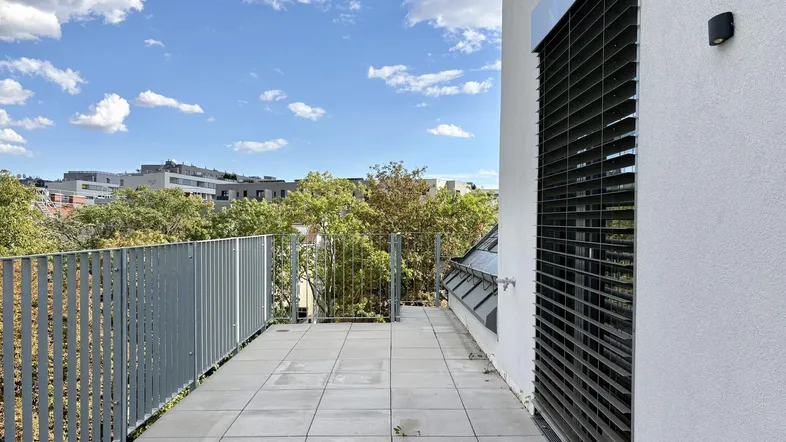 Geräumige Dachterrasse mit Fliesenboden, Metallgeländer und Blick ins Grüne.