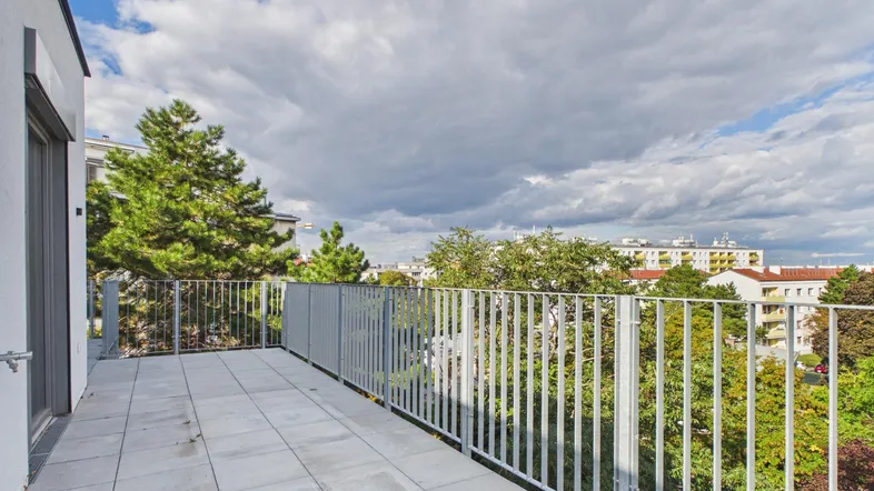 Große, geflieste Terrasse mit Metallgeländer und Blick auf Bäume und Gebäude.