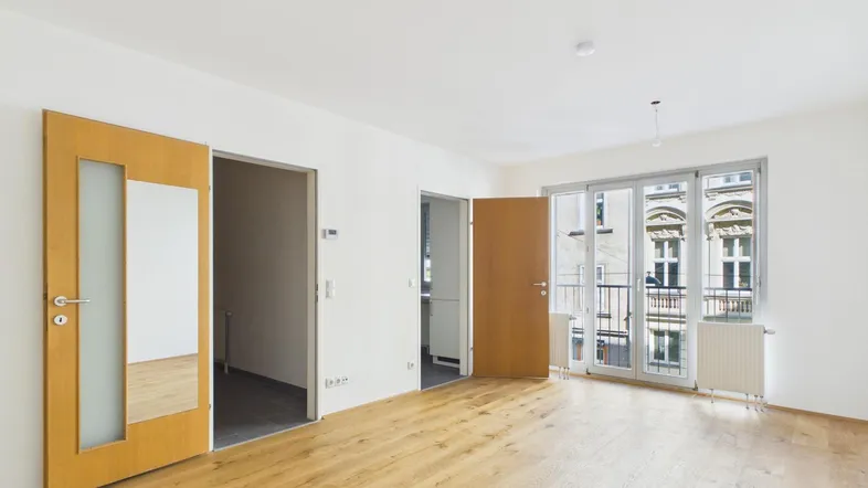 Helles, leeres Zimmer mit Parkettboden und Zugang zu einem französischen Balkon, ideal als Wohnzimmer.