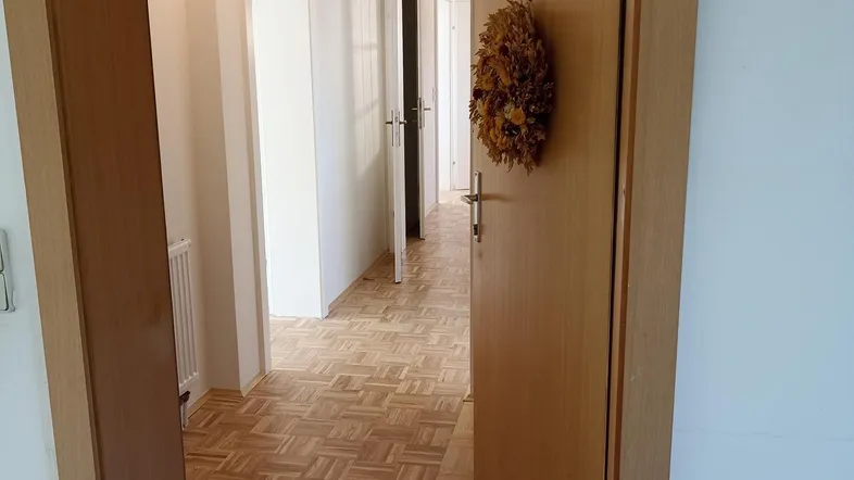 Langer Flur mit hellem Parkettboden, der zu weiteren Zimmern der Wohnung führt.