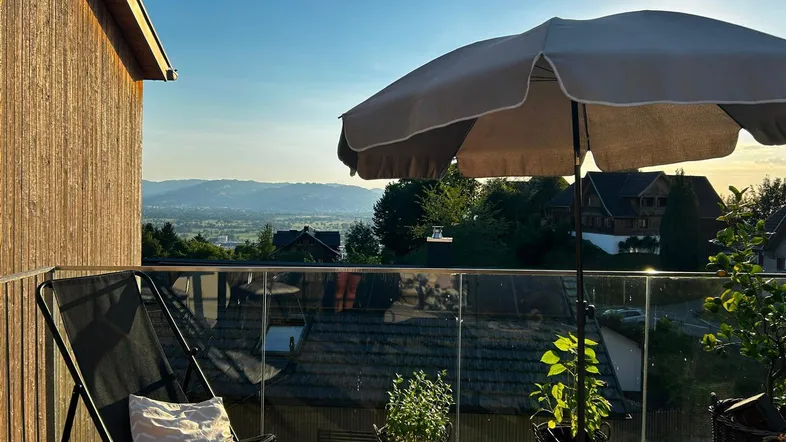 Gemütlicher Balkon mit Sitzgelegenheiten, Pflanzen und weitem Blick über die Landschaft bei Sonnenuntergang.