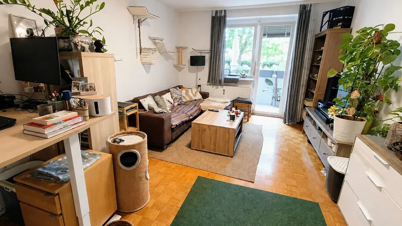 Helles Wohnzimmer mit Parkettboden, gemütlichem Sofa und Zugang zu einem kleinen Balkon.