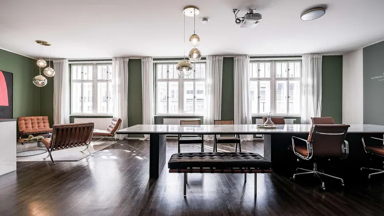 Großer Konferenzraum mit modernem Design, dunklem Holzboden, grünen Wänden und großen Fenstern für viel Tageslicht.