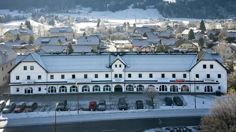 Gebäudeansicht im Winter mit schneebedecktem Dach und umliegender Landschaft.