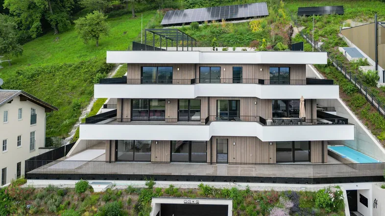 Moderne Wohnanlage am Hang mit Terrassen, Balkonen, Tiefgarage und Solaranlage.