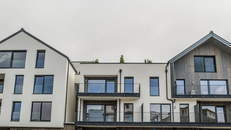 Moderne Wohngebäude mit heller Fassade, Holzverkleidung und mehreren Balkonen unter bewölktem Himmel.