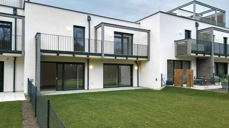 Moderne Reihenhäuser mit privaten Gärten und Balkonen, umgeben von Grünflächen.