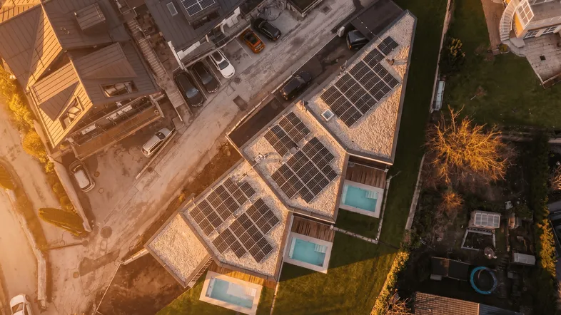 Luftaufnahme moderner Gebäude mit Solarpaneelen auf den Dächern und kleinen Pools im Gartenbereich bei Sonnenuntergang.