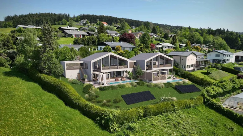 Eine Luftaufnahme zeigt zwei moderne Villen mit Pools und Solaranlagen in einer grünen Hügellandschaft.