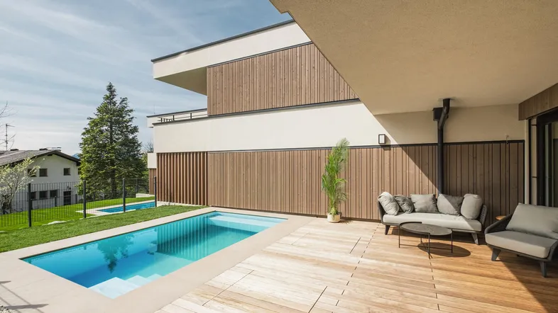 Geräumige Holzterrasse mit privatem Pool und gemütlicher Lounge-Sitzgruppe unter blauem Himmel.