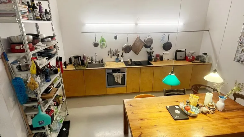 Offene Küche mit Holztisch und hohen Decken, integriert in einen hellen Wohnbereich.