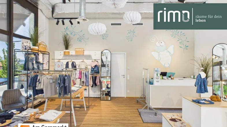Heller und moderner Verkaufsraum für Kinderbekleidung mit großen Fenstern und Holzboden.