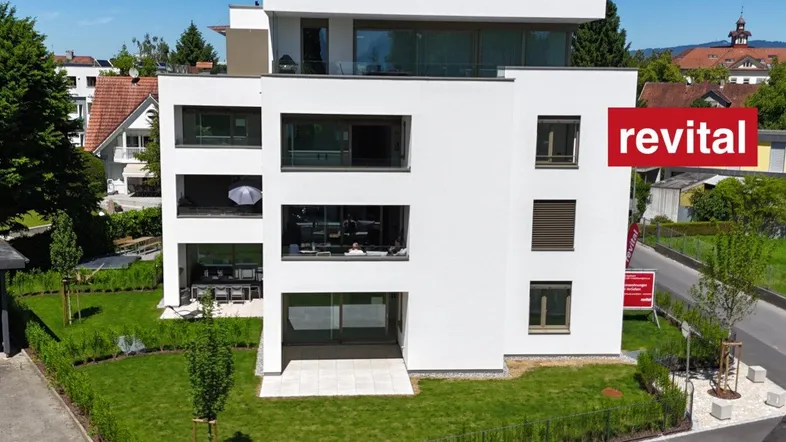 Modernes weißes Mehrfamilienhaus mit Balkonen und gepflegter Grünfläche in sonniger Umgebung.