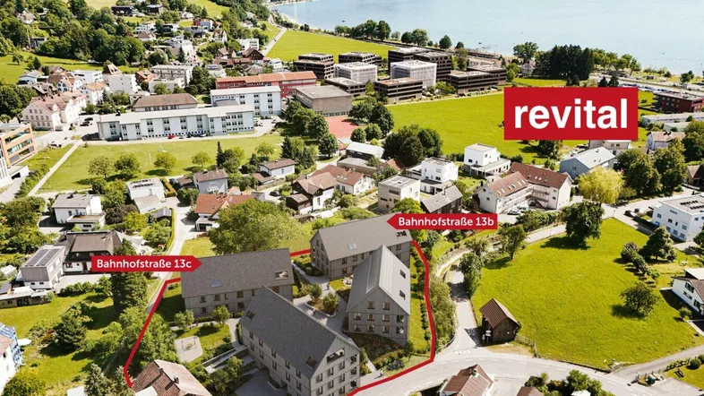Luftaufnahme der modernen Wohnanlage am Seeufer mit umliegender Natur und Bergen im Hintergrund.