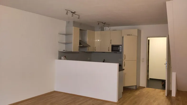 Heller offener Wohnbereich mit integrierter Küchenzeile und Parkettboden, ideal für modernes Wohnen.