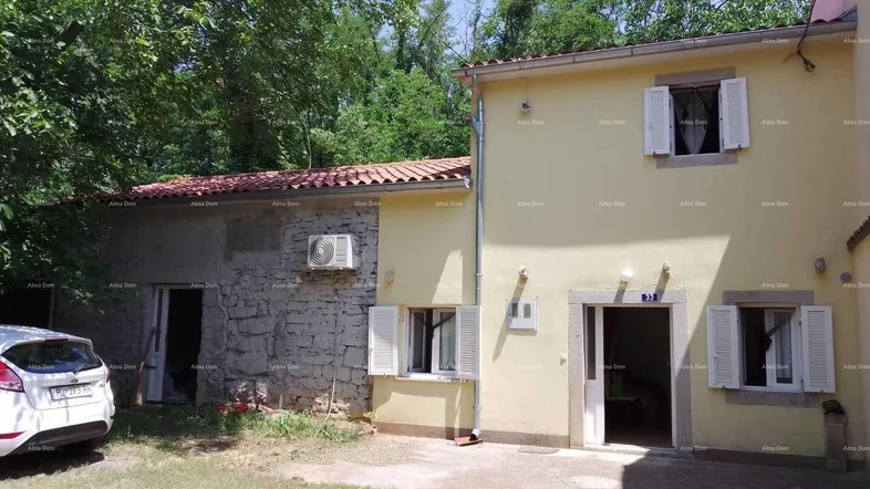 Außenansicht eines Hauses mit gelber Fassade und Steinelementen, umgeben von viel Grün.