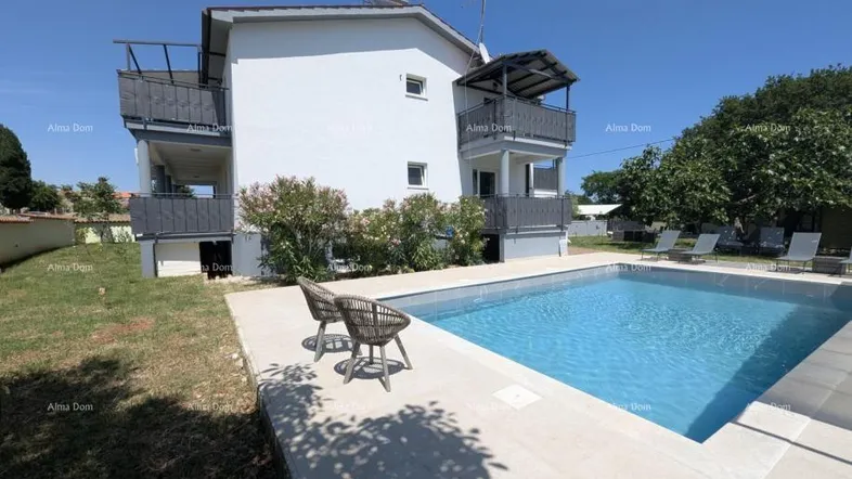 Außenansicht des Gebäudes mit großem Swimmingpool und sonniger Terrasse, umgeben von Grünflächen.