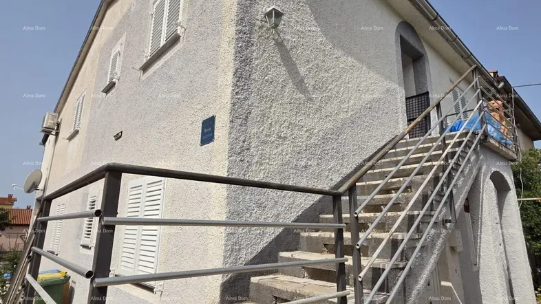 Außenansicht eines Gebäudes mit Außentreppe und weißer Putzfassade unter blauem Himmel.
