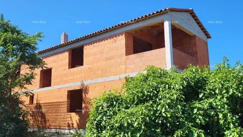 Rohbau eines Einfamilienhauses mit Ziegelwänden unter blauem Himmel, umgeben von Bäumen.