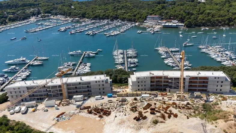 Luftaufnahme einer Baustelle mit zwei im Bau befindlichen Gebäuden direkt neben einem Yachthafen.