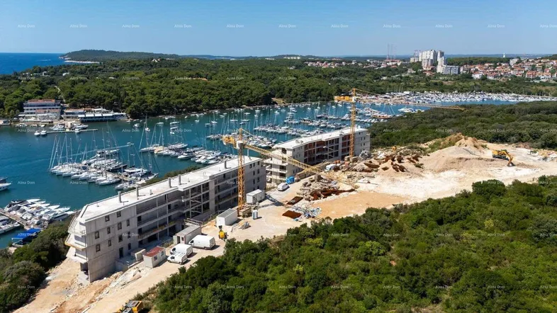 Luftaufnahme einer Baustelle mit im Bau befindlichen Gebäuden direkt an einem Yachthafen und dem Meer.