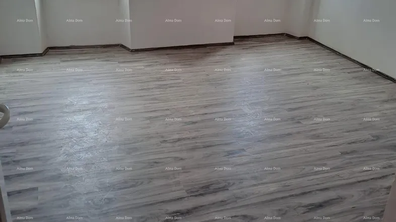 Helles Zimmer mit modernem Laminatboden und zwei Fenstern, die viel Tageslicht hereinlassen.