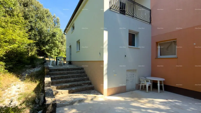 Seitenansicht des Gebäudes mit Außentreppe, kleiner Terrasse und umgebender Natur.