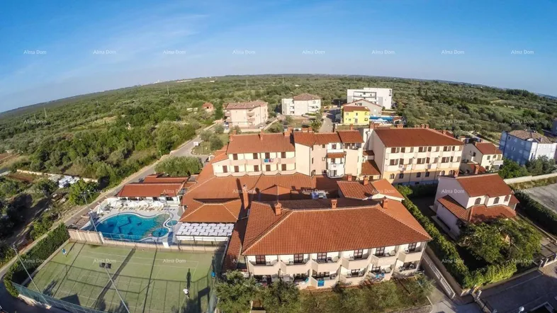 Luftaufnahme eines Hotelkomplexes mit mehreren Gebäuden, großem Poolbereich und Tennisplatz, umgeben von viel Grün.