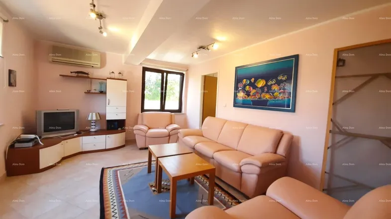 Helles Wohnzimmer mit beigefarbenen Sofas, Fliesenboden und Klimaanlage.