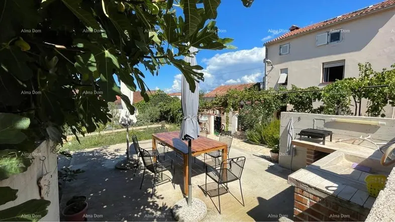 Sonniger Gartenbereich mit Esstisch, Sonnenschirm und gemauertem Grillplatz für entspannte Stunden im Freien.