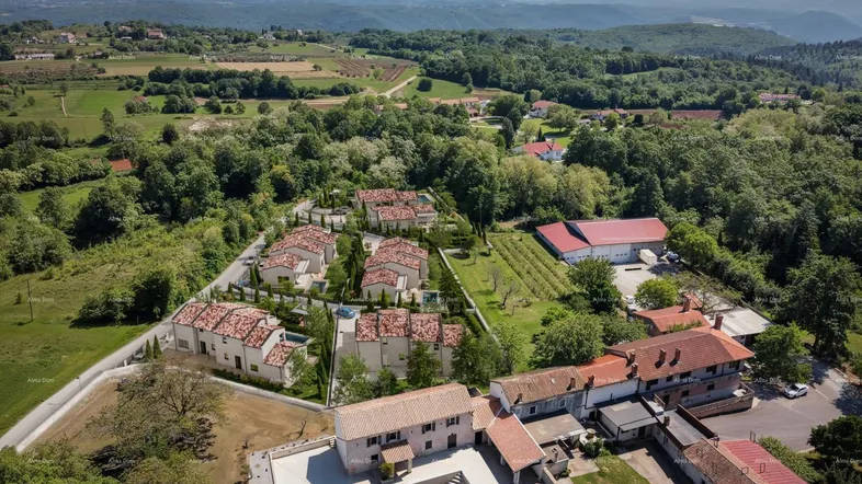 Luftaufnahme einer Wohnsiedlung mit mehreren Häusern und Pools in ländlicher Umgebung mit grünen Hügeln.