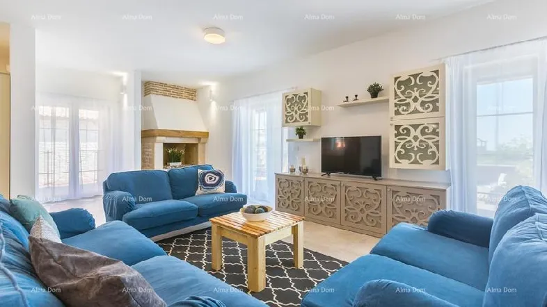 Helles Wohnzimmer mit blauen Sofas, Kamin und Zugang zur Terrasse durch große Fenster.