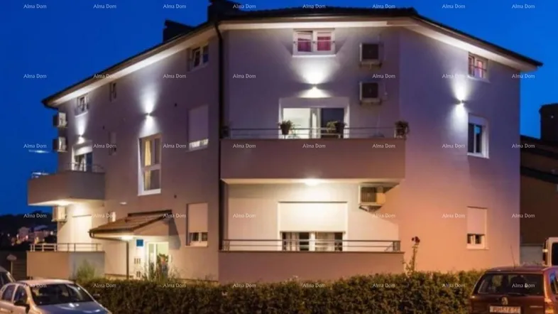 Modernes Mehrfamilienhaus bei Nacht mit beleuchteter Fassade und Rollläden an den Fenstern.