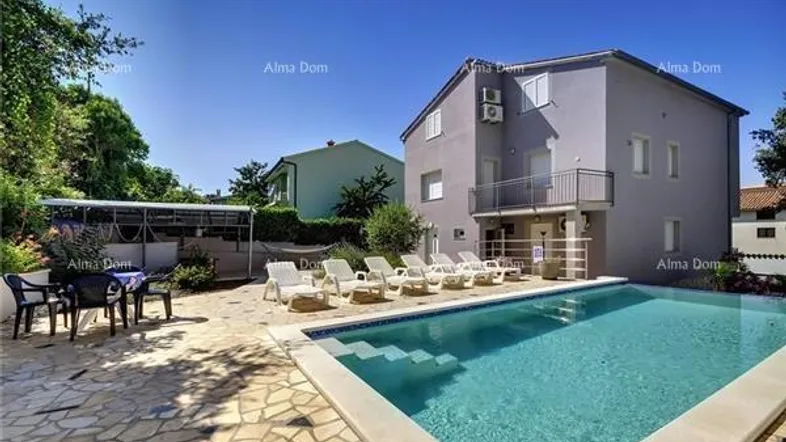 Außenbereich mit großem Pool, Sonnenliegen und angrenzendem Gebäude unter blauem Himmel.