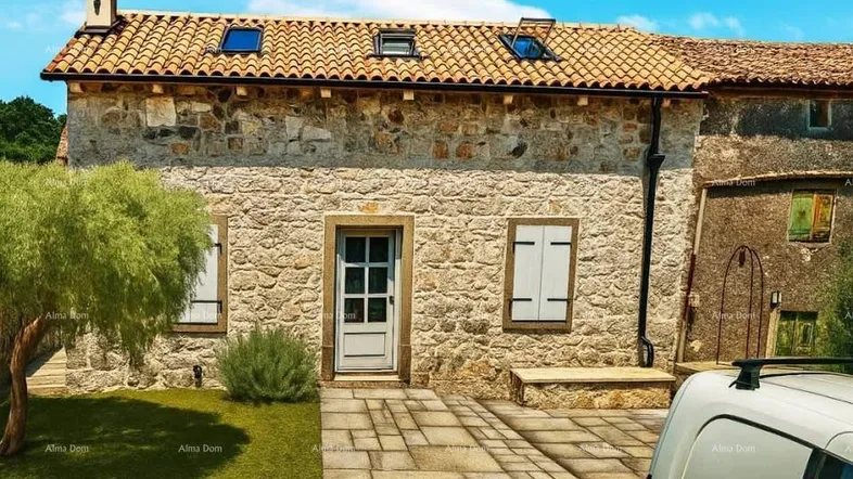 Traditionelles Steinhaus mit Ziegeldach und Fensterläden, umgeben von einem kleinen Vorgarten.