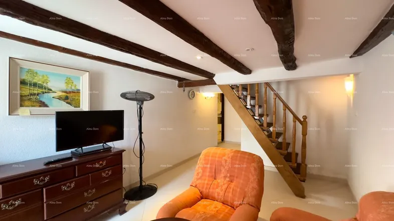 Gemütliches Wohnzimmer mit sichtbaren Holzbalken, traditionellen Möbeln und einer Holztreppe zum Obergeschoss.