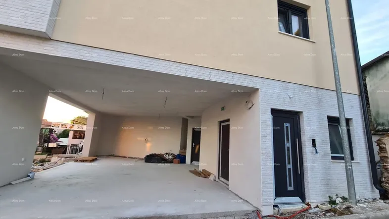 Neubau mit moderner Fassade, Eingangsbereich und überdachtem Parkplatz im Bauzustand.