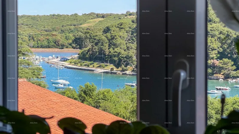 Blick aus einem Fenster auf eine malerische Bucht mit Booten und grünen Hügeln unter blauem Himmel.