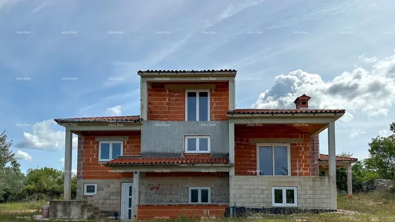 Haus im Rohbau mit Ziegelwänden und Dachziegeln unter blauem Himmel.