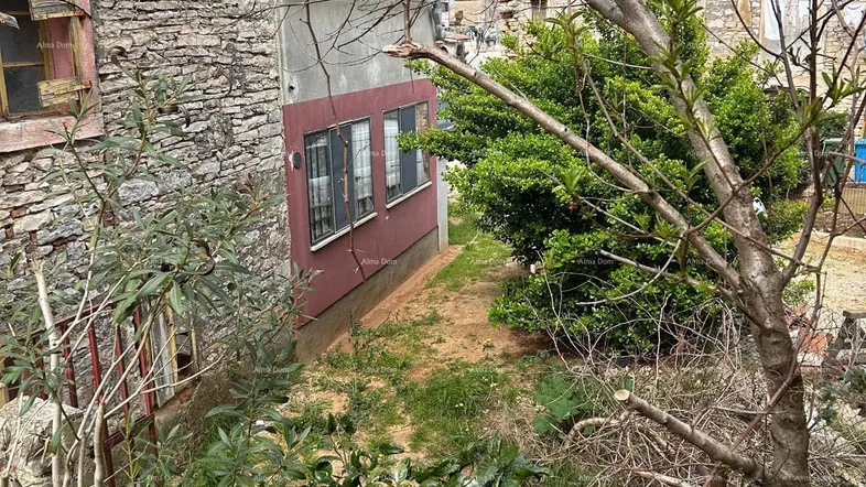 Schmaler Durchgang zwischen alten Steinhäusern mit üppiger Vegetation.