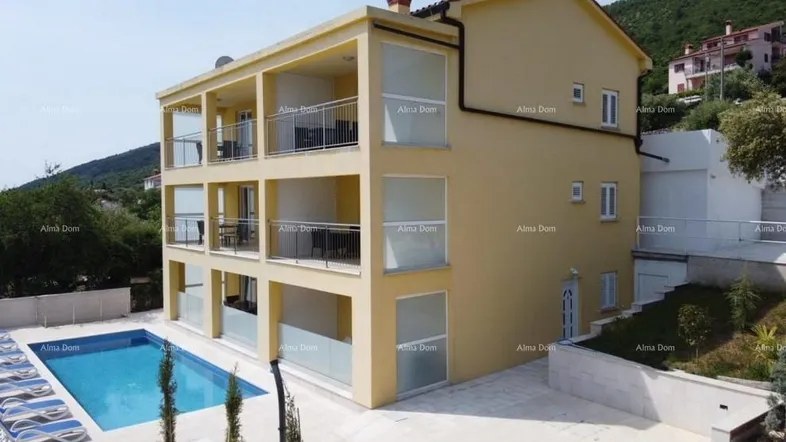 Modernes Apartmentgebäude mit mehreren Balkonen, großem Poolbereich und Liegestühlen.