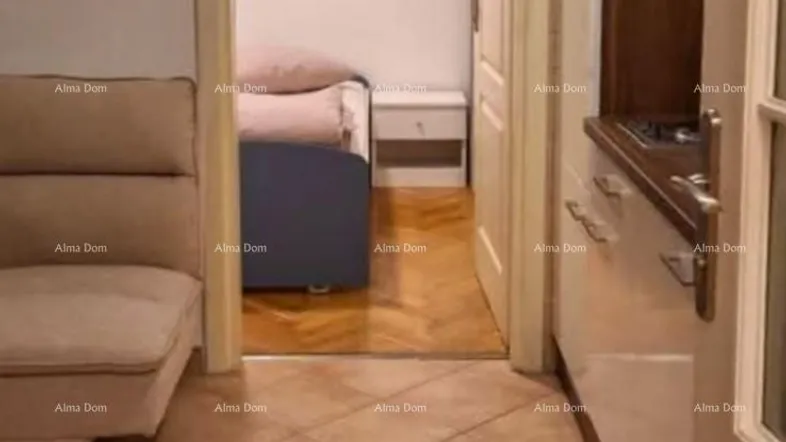 Blick von einem gefliesten Bereich mit Sofa und Küchenzeile in ein angrenzendes Schlafzimmer.