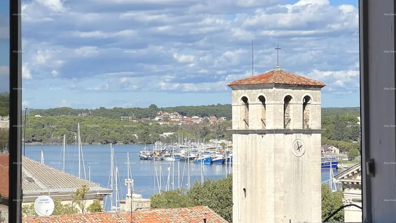 Blick aus dem Fenster auf den Hafen mit Booten und einem historischen Glockenturm unter blauem Himmel.